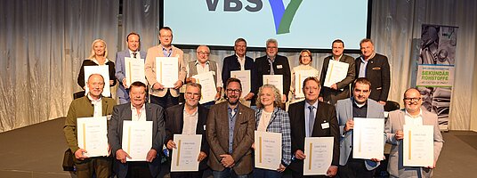 17 Menschen mit einer Urkunde stehen vor dem Schriftzug 50 Jahre VBS